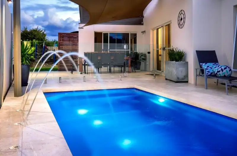 Moderne hus med swimmingpool i baghaven ved solnedgang, fokus på poolens belysning.