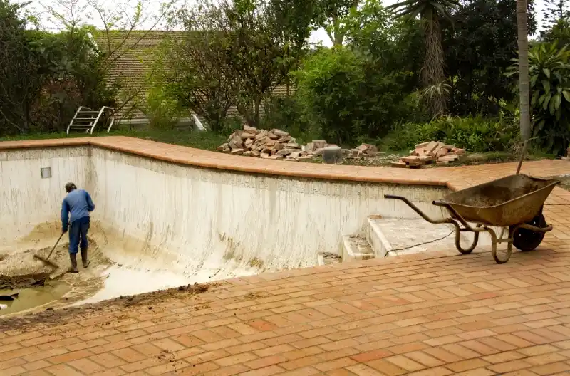 Mand renoverer udendørs poolbelægning med værktøj i solrigt vejr